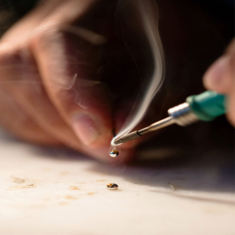 An artisan carefully soldering a small jewelry component, showcasing the meticulous craftsmanship behind every Abellé 18K gold-plated, hand-painted cross necklace.